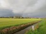 Naderende regenbui boven Goënga. De nog schijnende zon zorgt voor een beginnende regenboog.