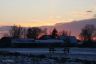 De zon laat boven het dorp Goënga een paars-roze hemel achter.
Op de voorgrond het kaatsveld met de kantine van K.F. De Legean.